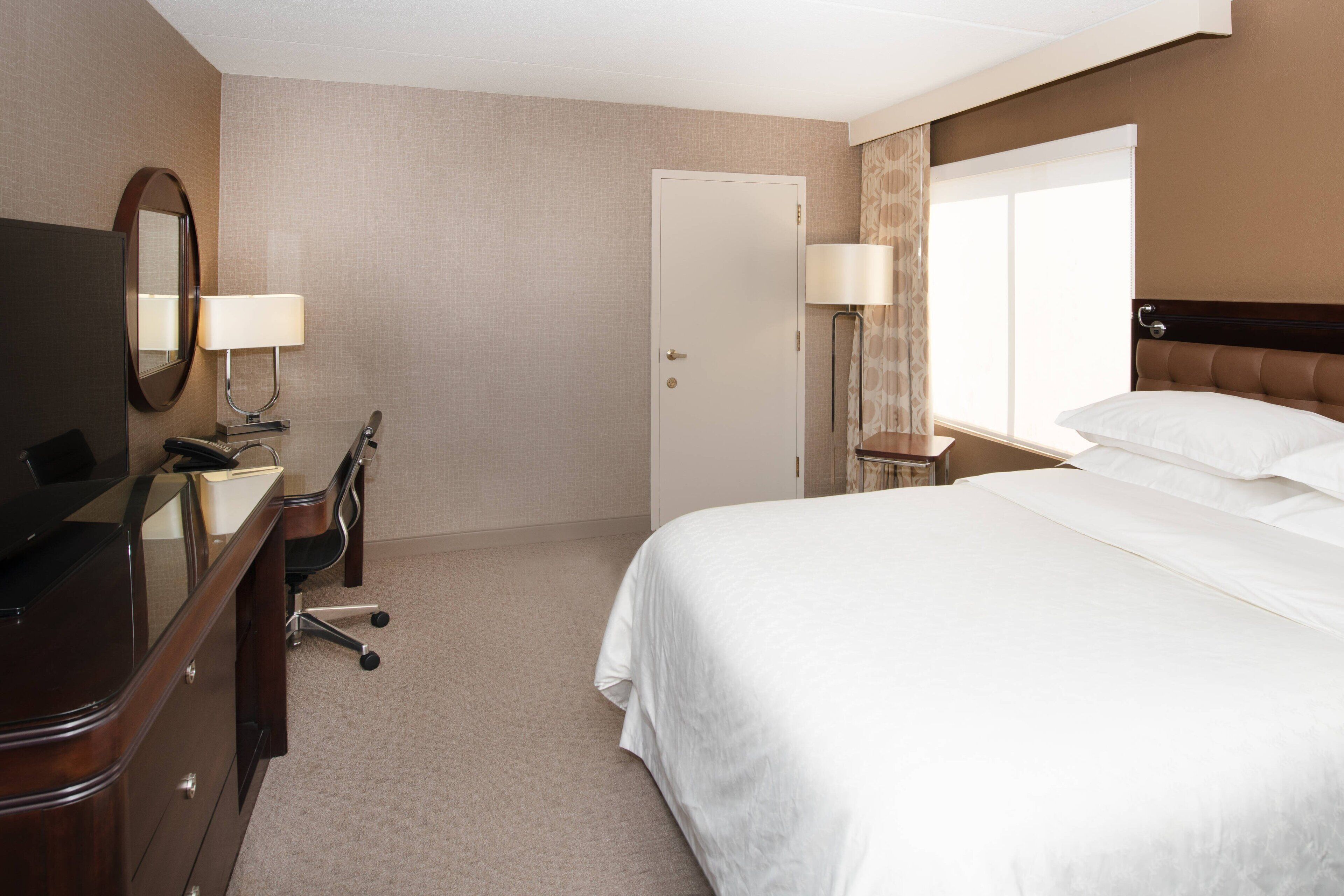 A hotel room with a bed, a desk with a chair, a TV, and a door.