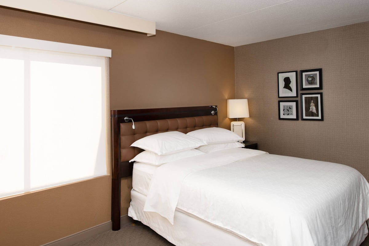 A hotel room with a large bed, a nightstand with a lamp, and a wall with framed pictures.