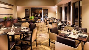 A spacious dining area with multiple tables set for guests, featuring a patterned carpet and modern furnishings.