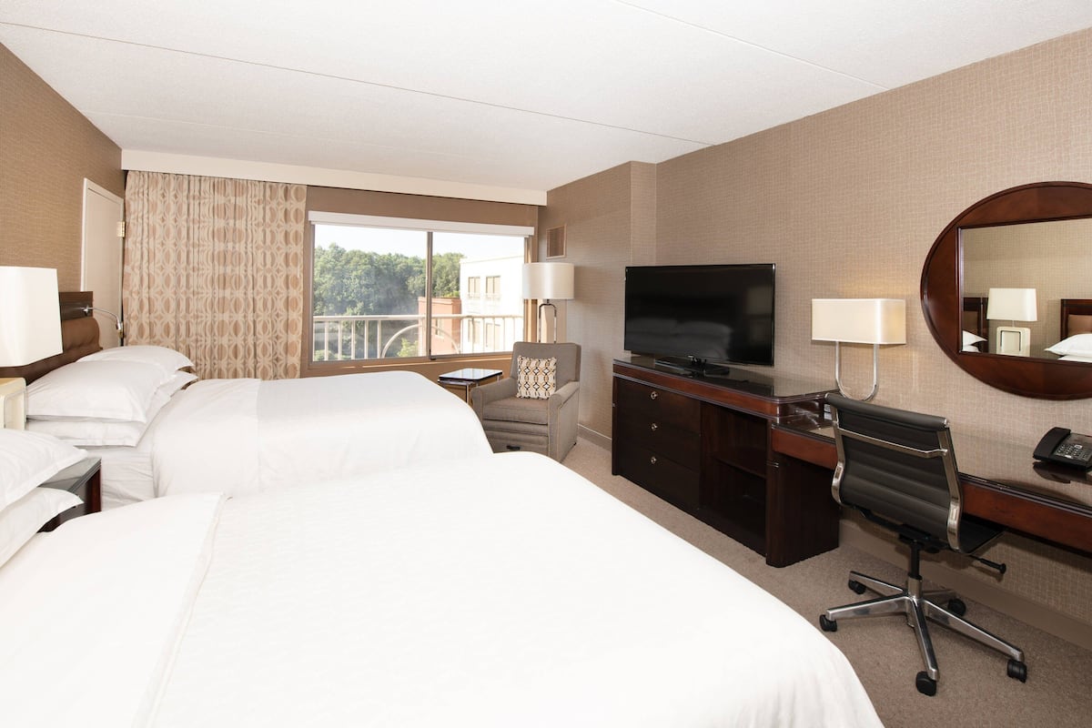 A hotel room with two beds, a desk, a chair, a TV, and a balcony view.