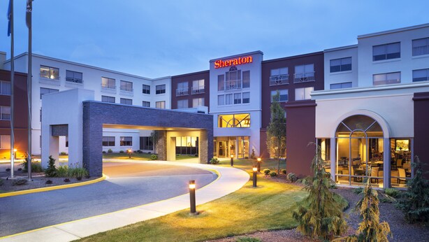 A Sheraton hotel with a modern design, featuring a prominent entrance, well-lit pathways, and landscaped surroundings.