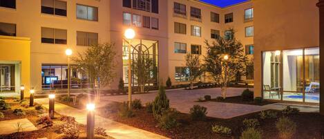 Un hotel de varios pisos con un patio, iluminación exterior y un jardín bien cuidado.