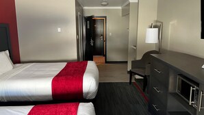 A hotel room with two beds, a desk, a chair, and a microwave. - Yukon Inn (Whitehorse)
