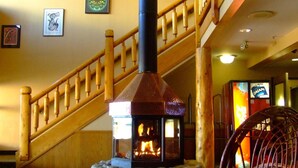 A stone fireplace with a glass enclosure, a wooden staircase, and a wicker chair. - Yukon Inn (Whitehorse)