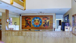 A reception desk with a wooden finish and a large indigenous artwork above it. - Yukon Inn (Whitehorse)