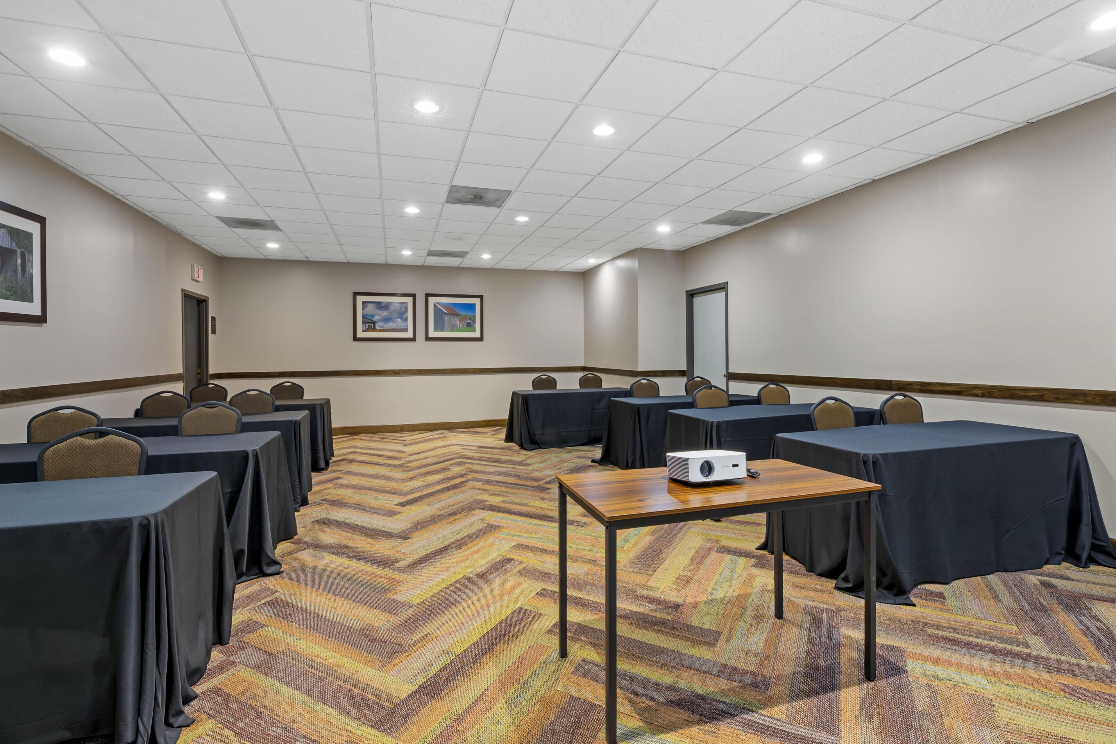 A conference room with tables, chairs, a projector, and a carpeted floor.