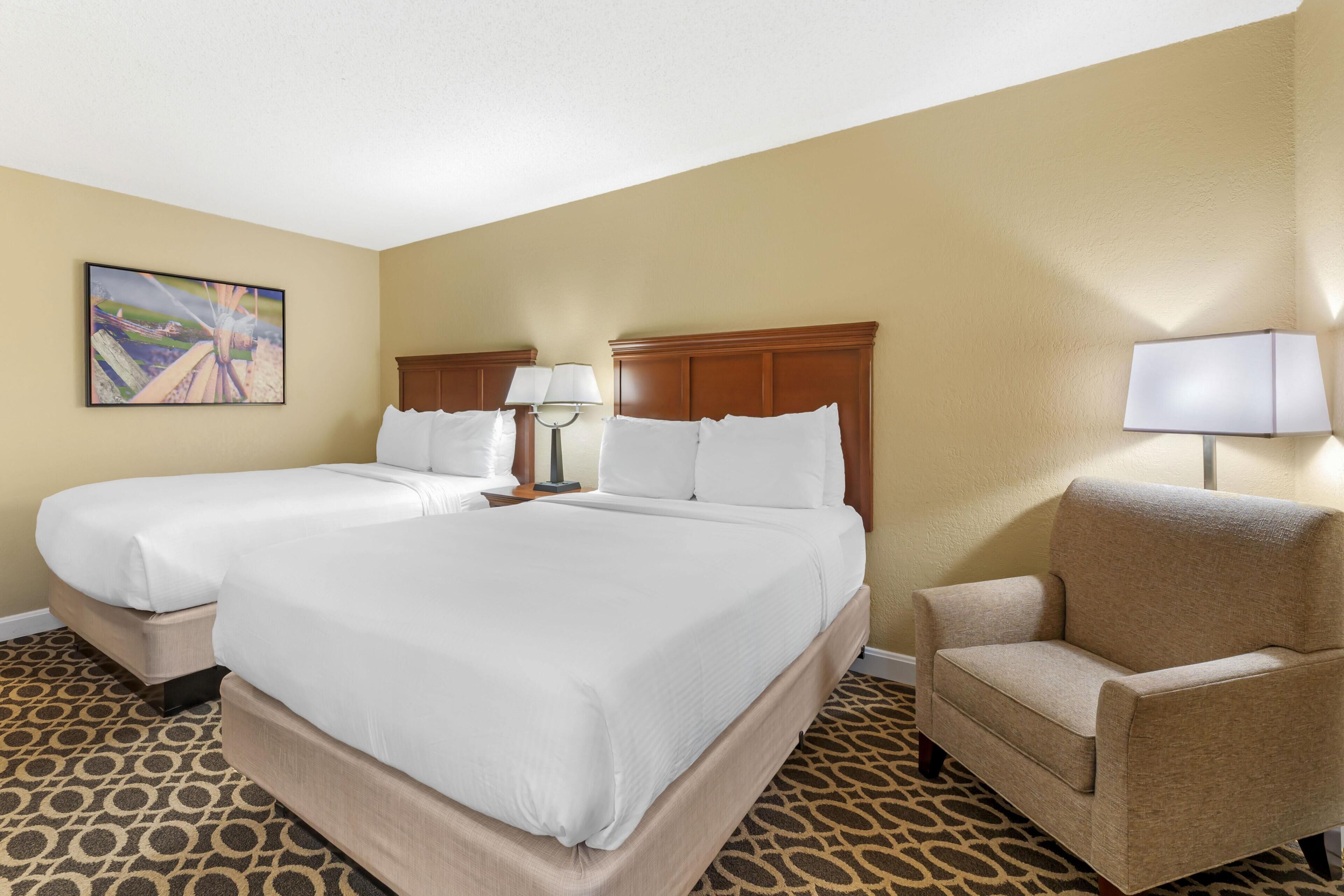 A hotel room with two beds, a sofa, a lamp, and a painting on the wall.