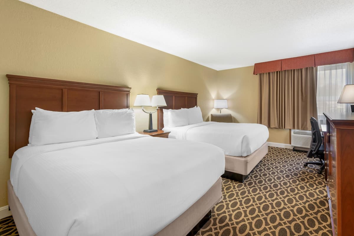 A hotel room with two beds, a desk, a chair, and a window with curtains.