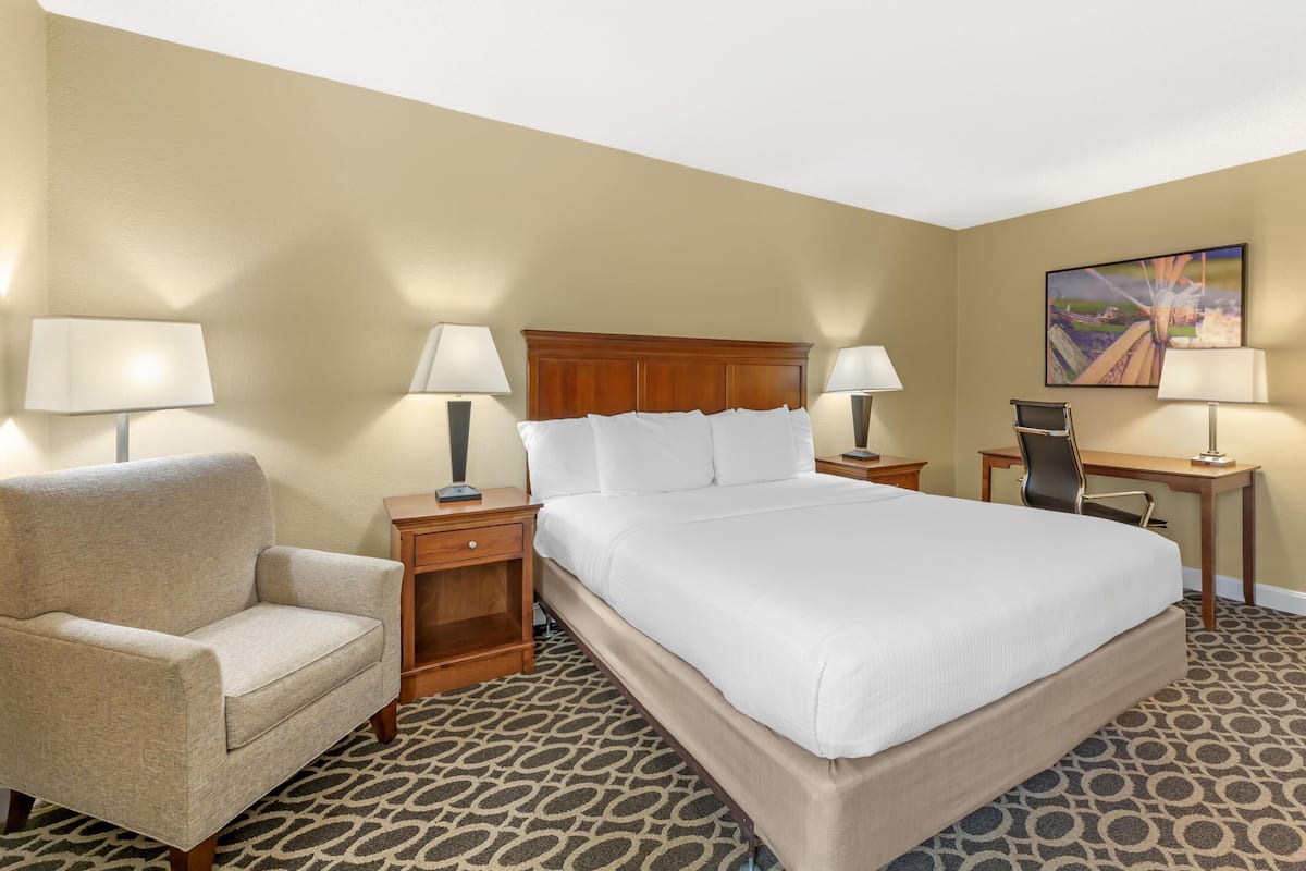 A hotel room with a large bed, a chair, a desk, and a painting on the wall.