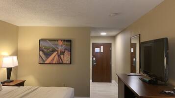 A hotel room with a bed, a desk with a computer, a TV, a lamp, and a painting on the wall.