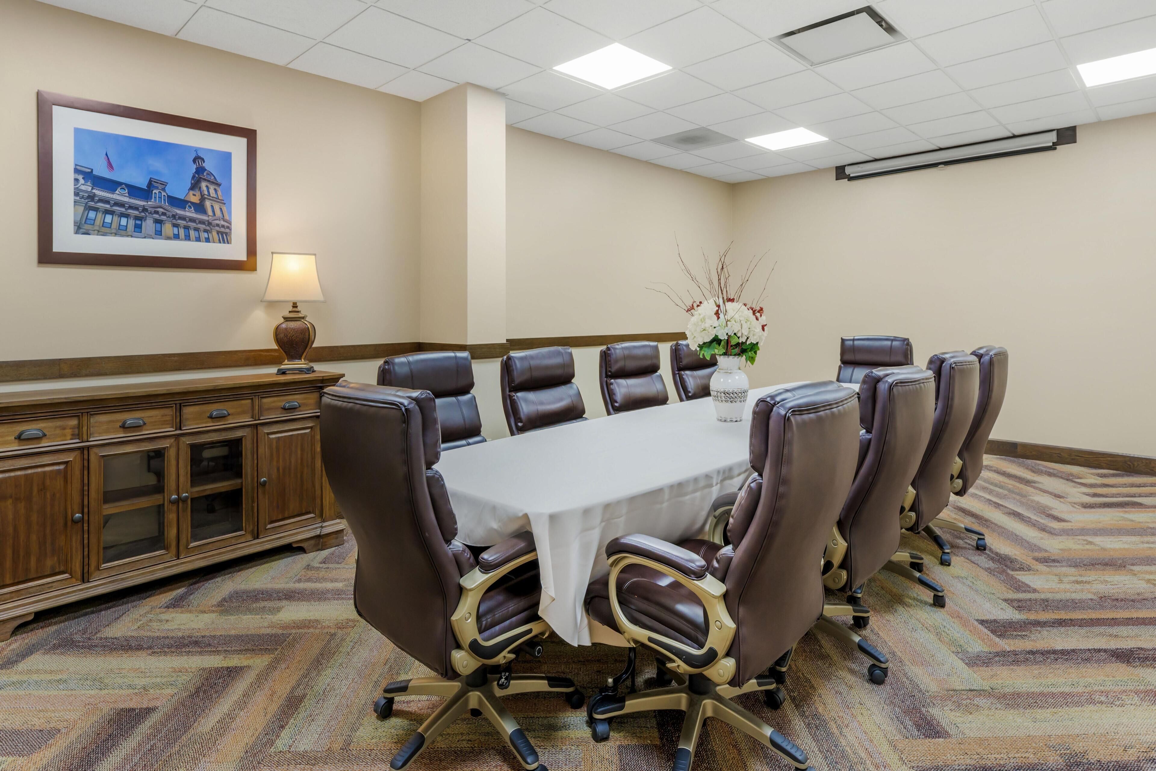 A conference room with a large table, leather chairs, a wooden cabinet, and a framed picture on the wall.