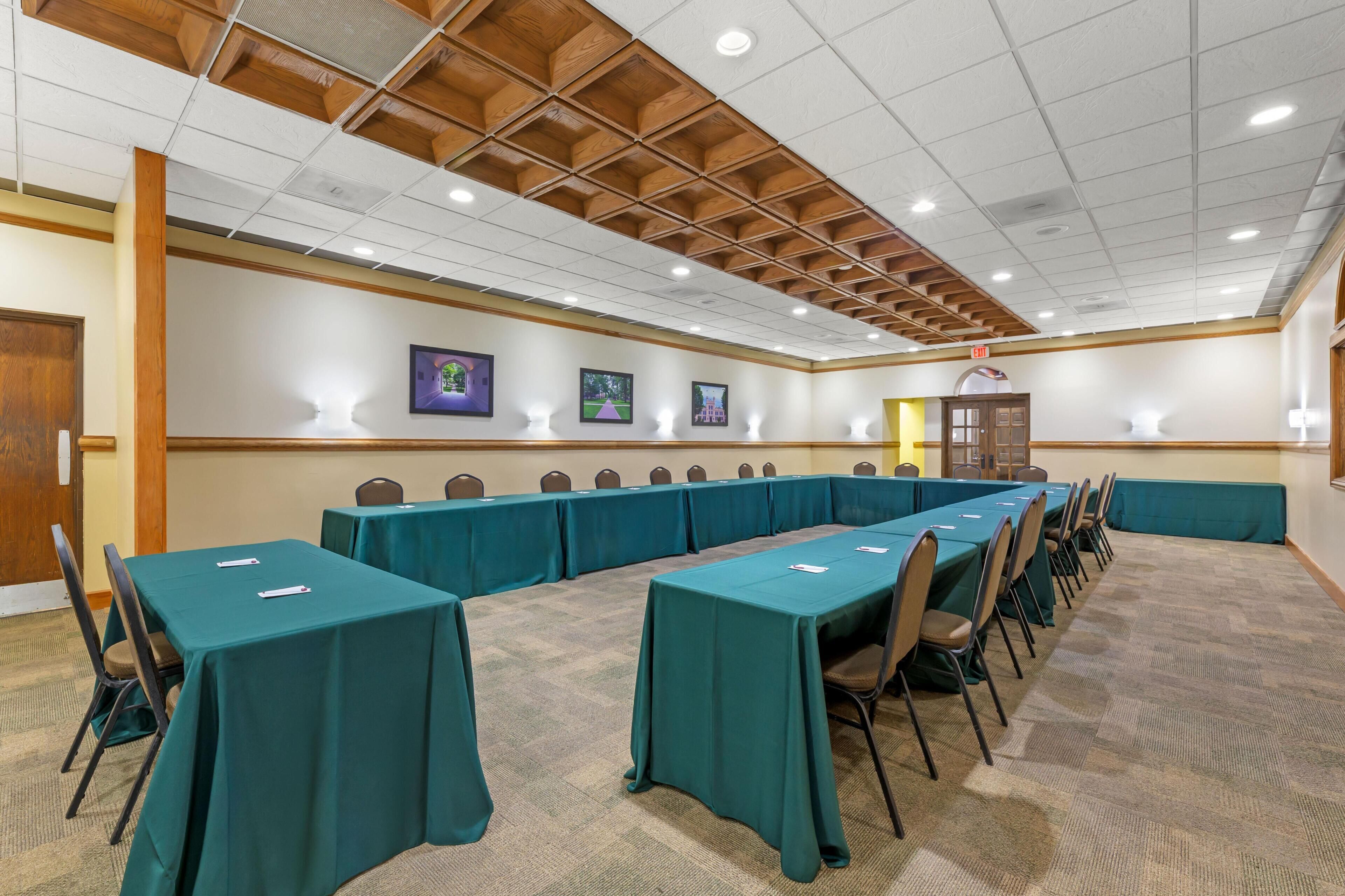 Une salle de conférence avec de longues tables et des chaises, des poutres en bois au plafond et des tableaux encadrés accrochés aux murs.