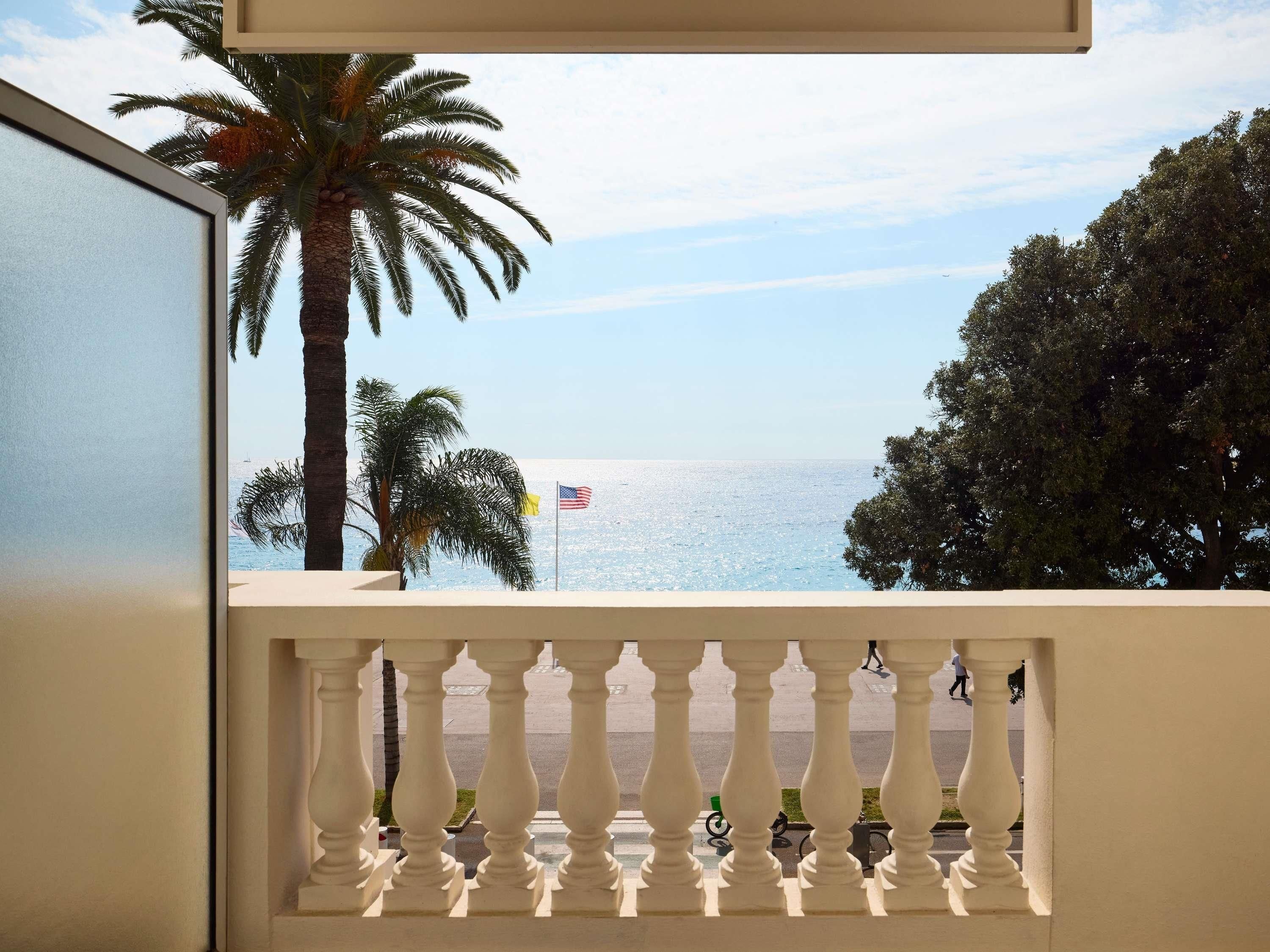 Varanda com vista para o mar, palmeiras e uma bandeira.