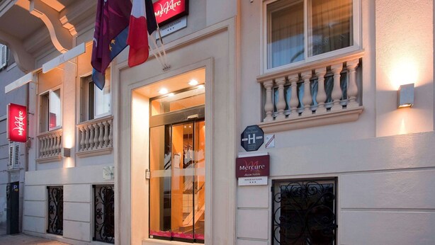 A hotel facade with a sign indicating it is a Mercure hotel, a sign for hotel tourism, and a flag. - Mercure Nice Marche aux Fleurs (Nice)