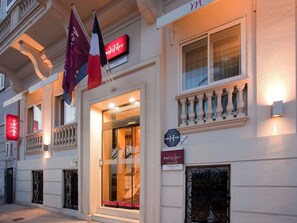 A hotel facade with a sign indicating it is a Mercure hotel, a sign for hotel tourism, and a flag. - Mercure Nice Marche aux Fleurs (Nice)