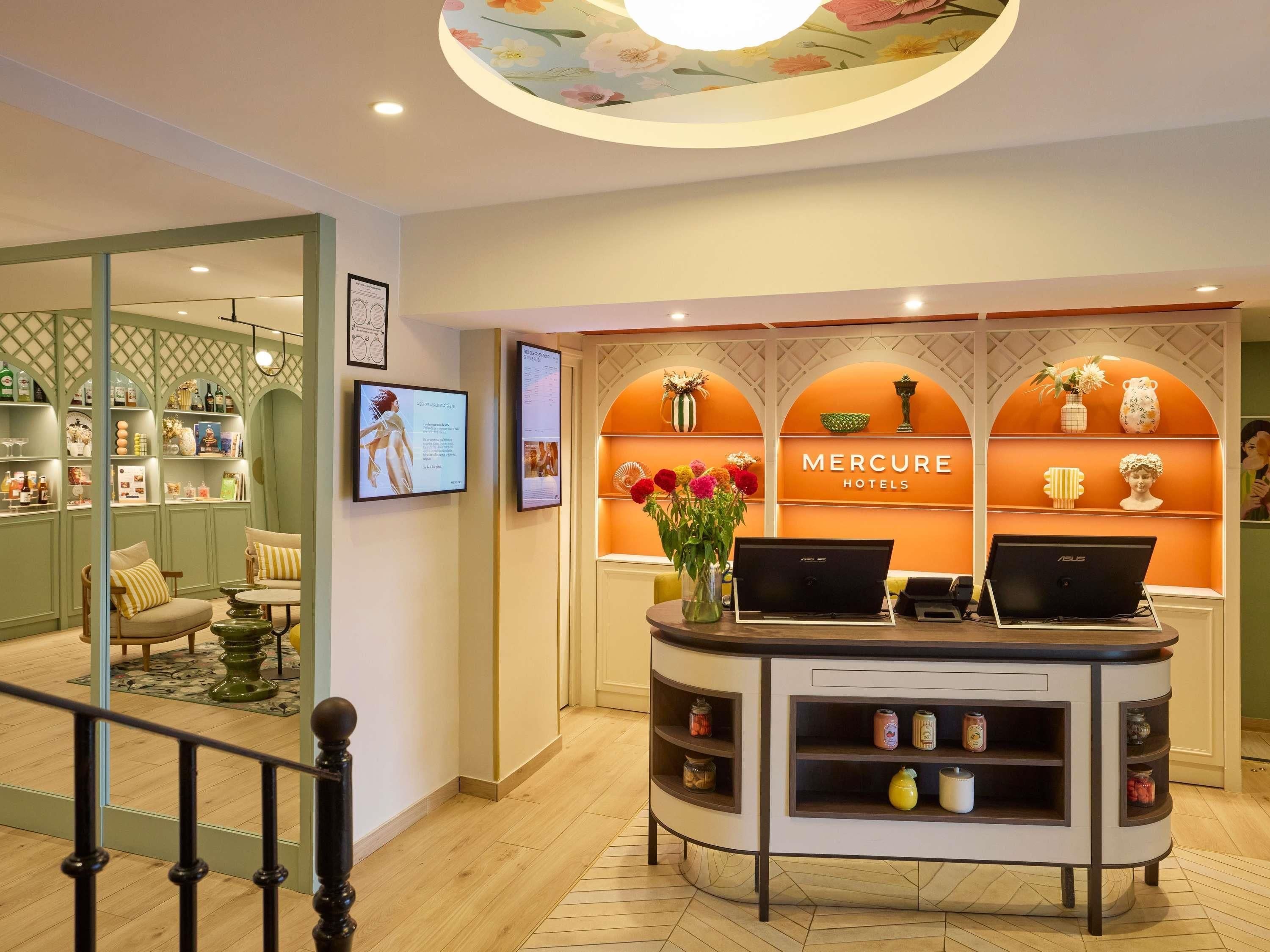 Un comptoir d’accueil avec un ordinateur portable, un vase rempli de fleurs et un mur orné d’une fresque florale.