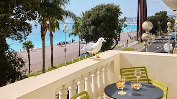 A balcony with a table and chairs, overlooking a beach and promenade with people and a seagull.