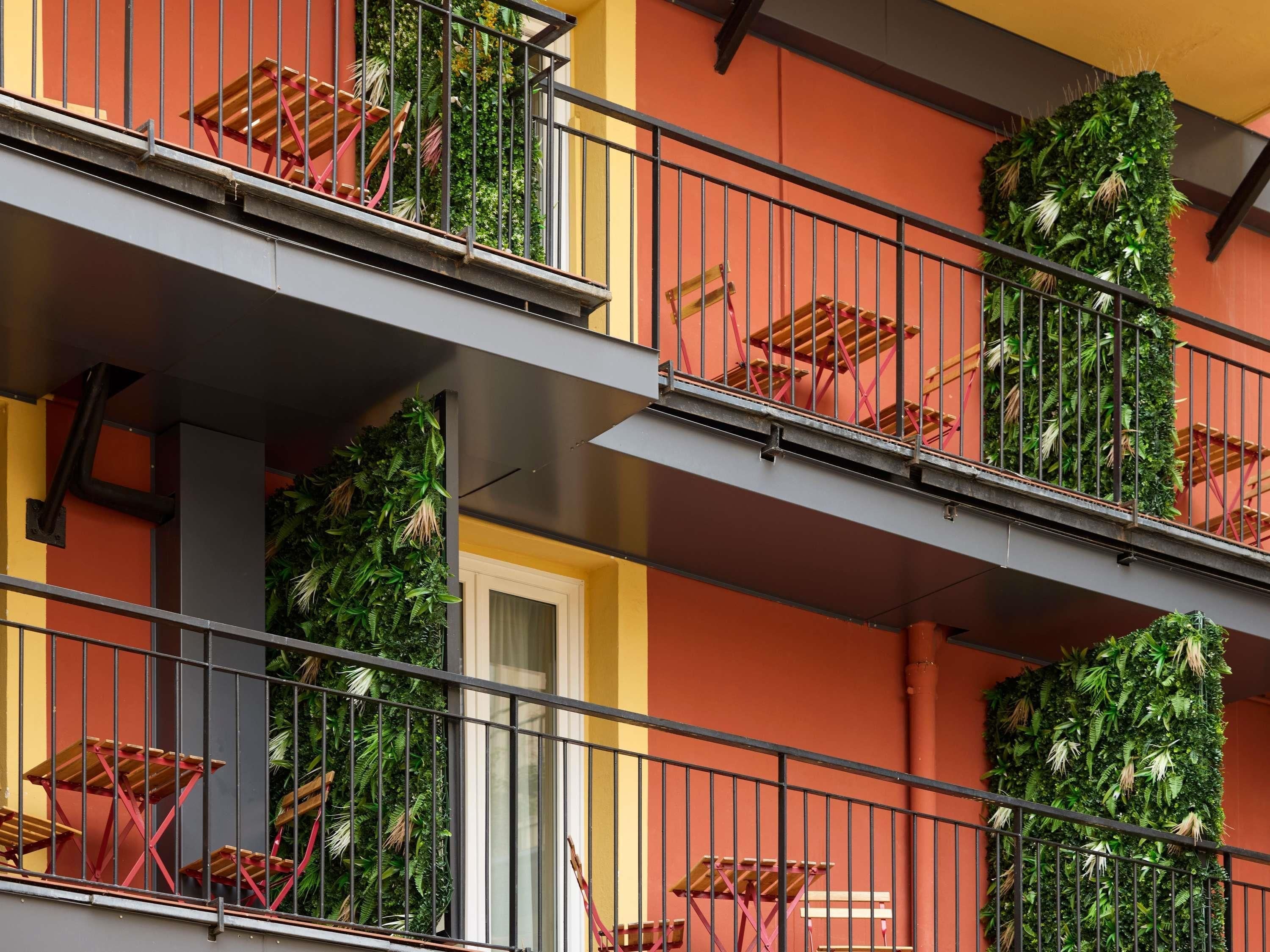 Un edificio de varios pisos con balcones, algunos con barandillas de metal y otros con plantas.