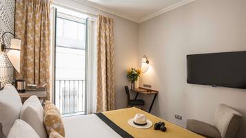 Une chambre d’hôtel avec un lit, un bureau avec une lampe, une chaise, un téléviseur et une vue sur l’extérieur.