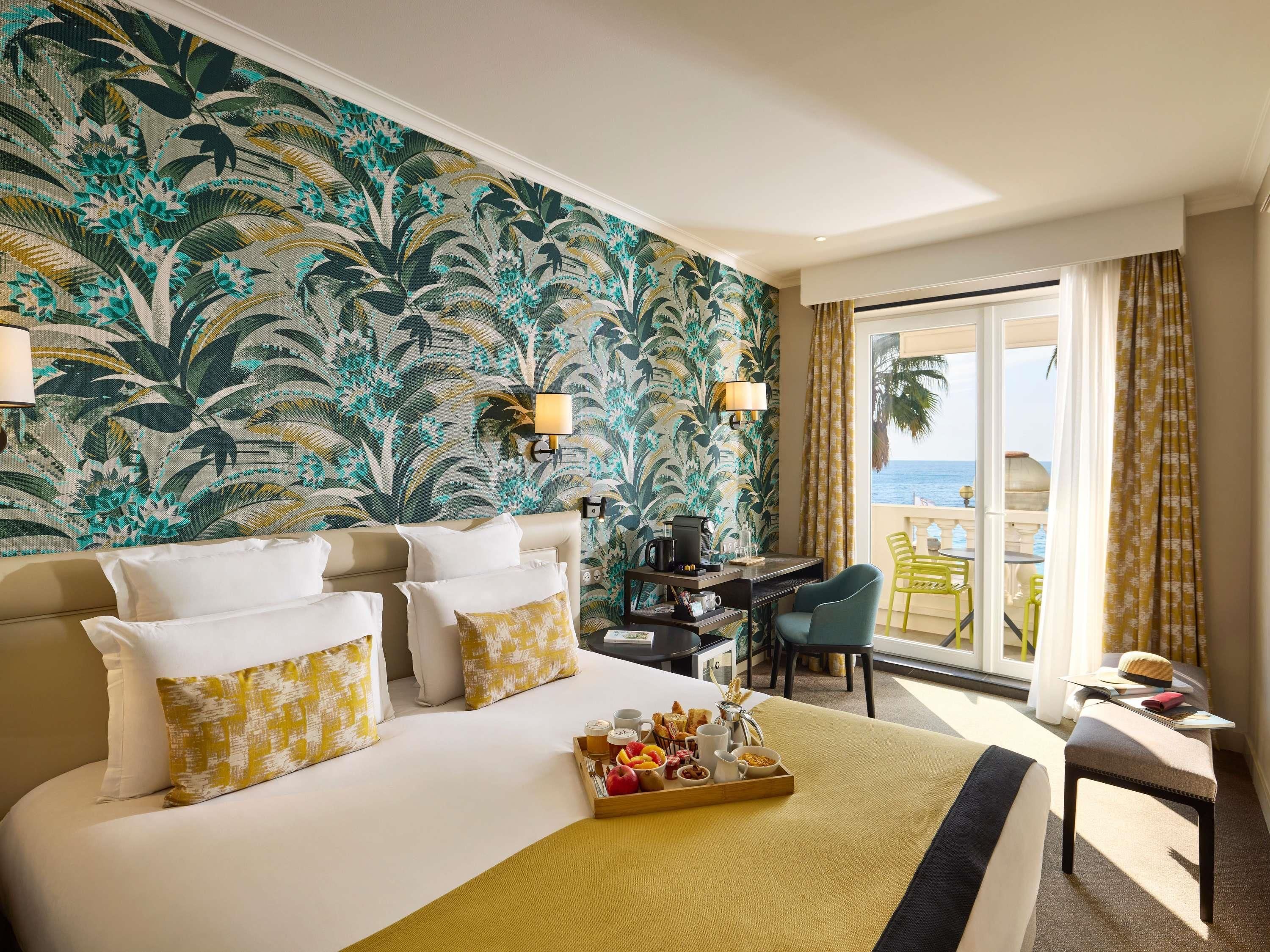 Habitación de hotel con una cama grande, un escritorio, una silla y un balcón con vista al mar.