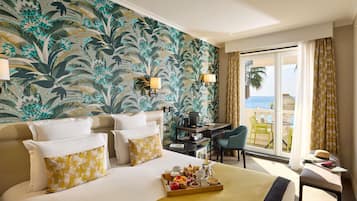 Habitación de hotel con una cama grande, un escritorio, una silla y un balcón con vista al mar.