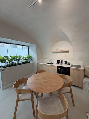 A modern kitchen with a dining area, featuring a round wooden table and chairs, a built-in oven, and a window with a view of greenery. - Mercure Nice Marche aux Fleurs (Nice)
