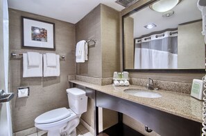 A bathroom with a toilet, sink, and mirror. There are towels hanging on a rack and a framed picture on the wall.