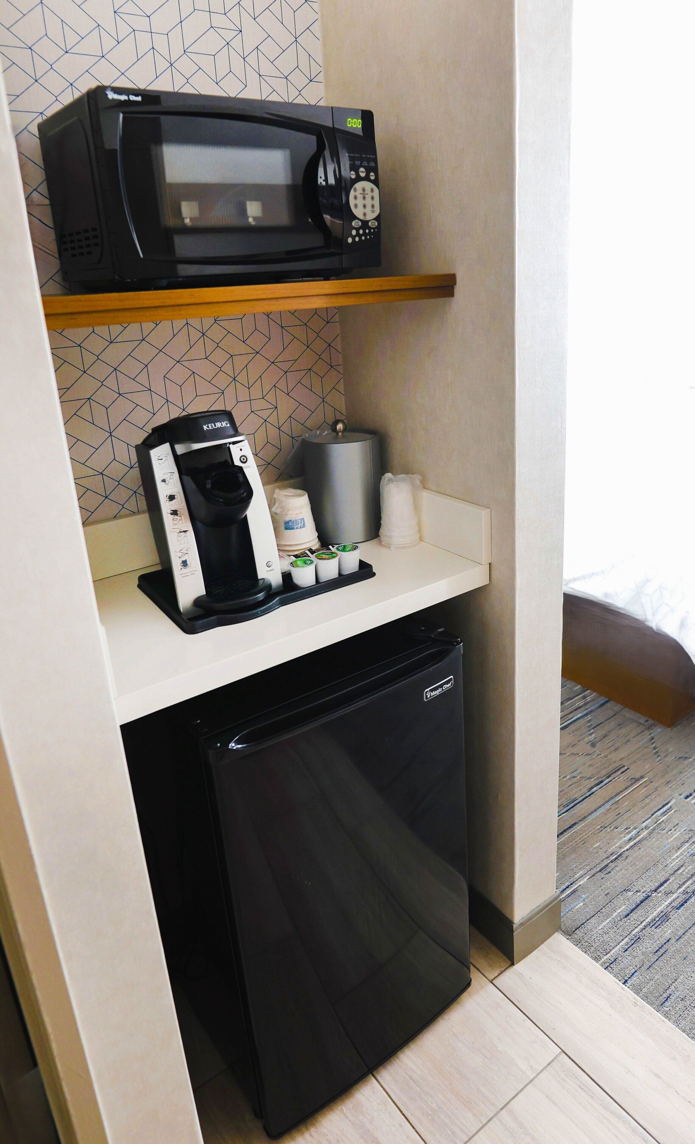Una kitchenette compacta con microondas, cafetera y un refrigerador pequeño.