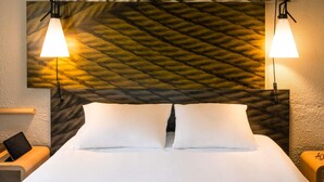 Una cama bien hecha con sábanas blancas, dos lámparas de noche y una pared con textura.