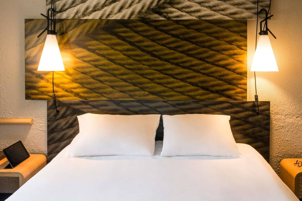 Una cama bien hecha con sábanas blancas, dos lámparas de noche y una pared con textura.