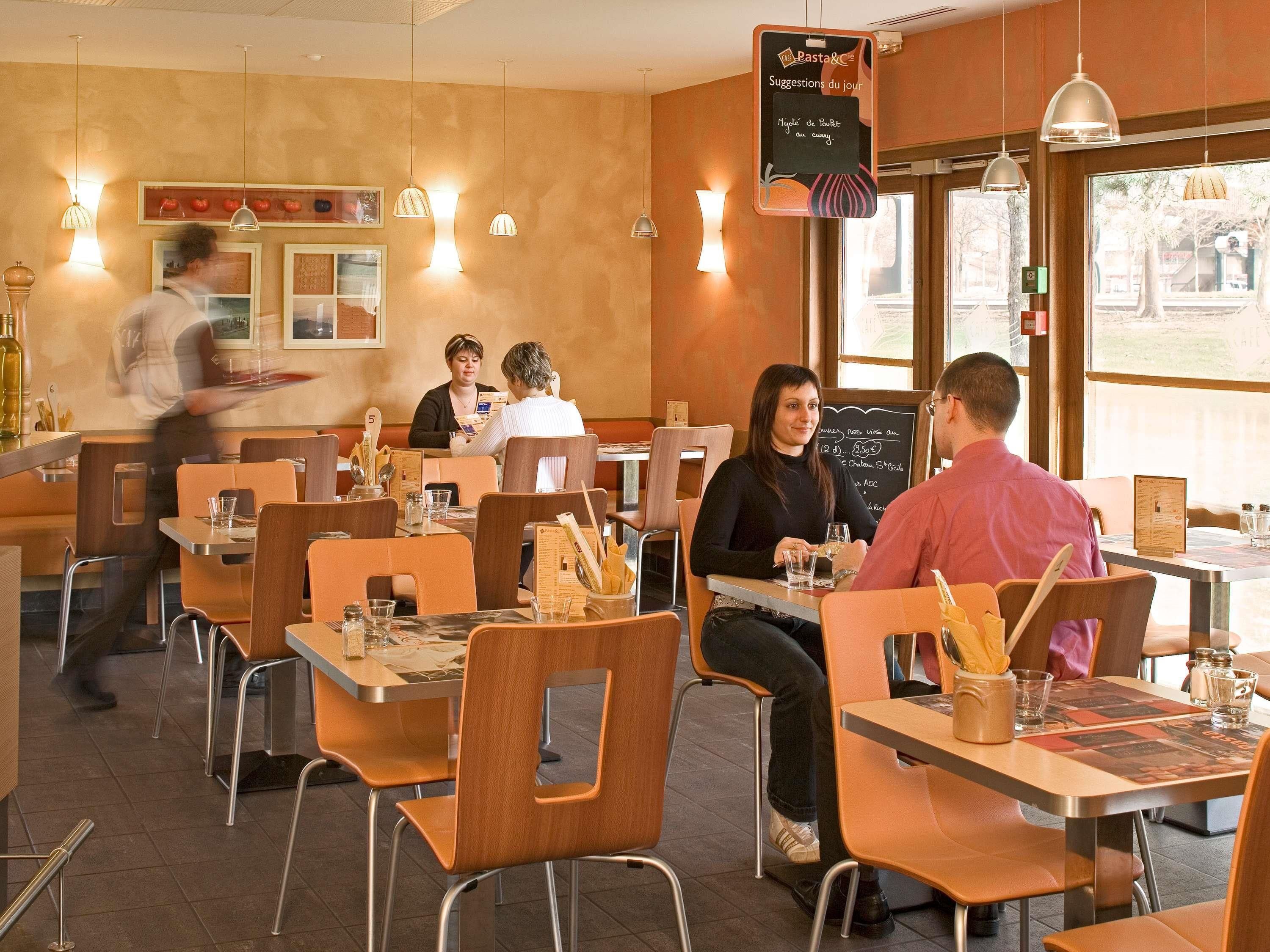 A restaurant interior with tables, chairs, and hanging pendant lights.