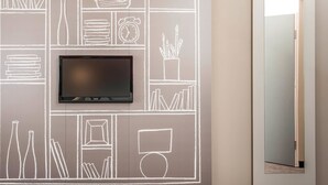 A modern room with a flat-screen TV mounted on a chalkboard wall, a door with a mirror, and a light fixture above it. - ibis Bourg En Bresse (Bourg-en-Bresse)