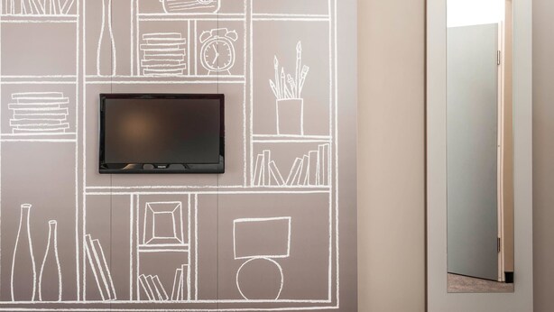 Una habitación moderna con televisión de pantalla plana montada en una pared de pizarra, una puerta con espejo y una lámpara colgante sobre ella.