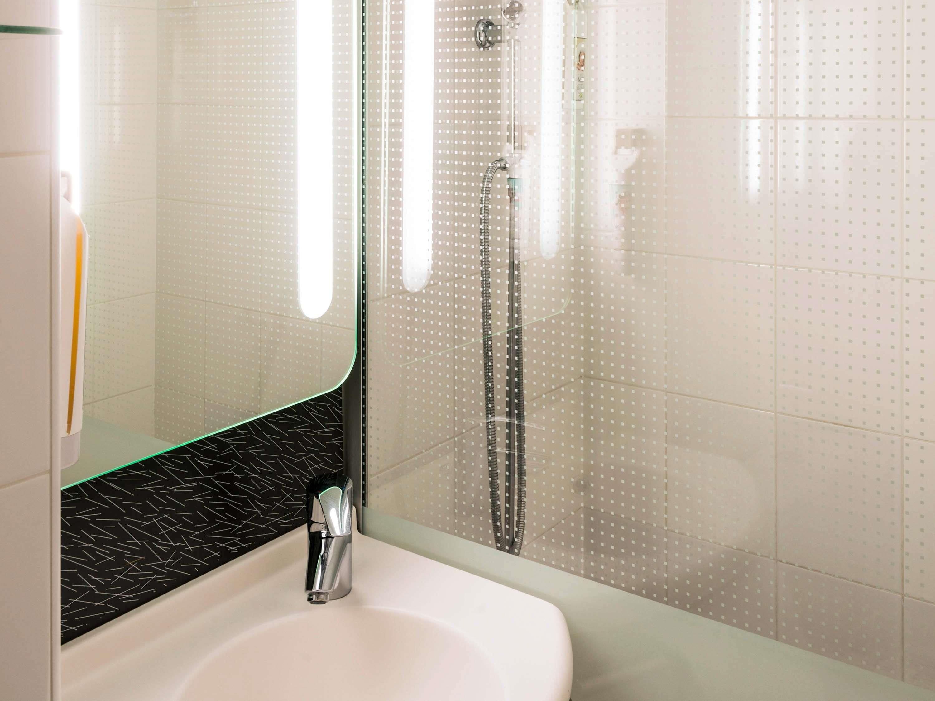 A modern bathroom with a white sink, a glass shower enclosure, and a black patterned backsplash.
