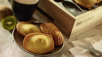 A plate of pastries, a cup of coffee, and a wooden box labeled 'ibis kitchen' on a table.