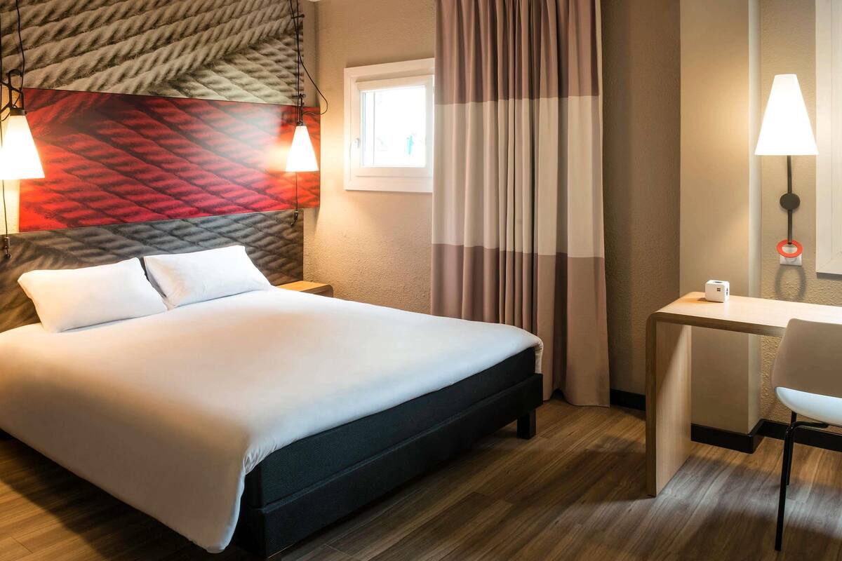 Una habitación de hotel con cama, escritorio, silla y lámpara.