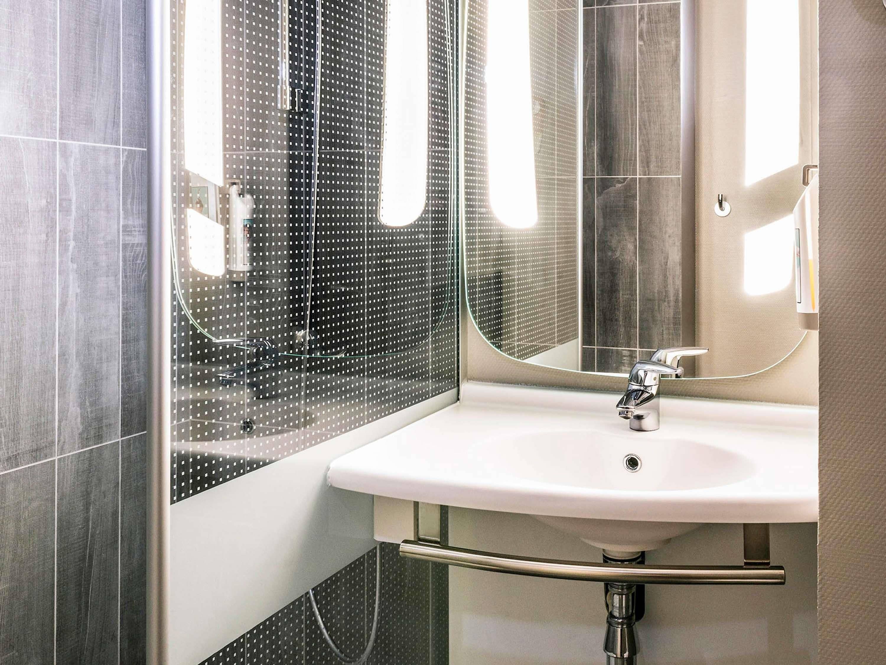 Un baño moderno con un espejo grande, un lavamanos blanco y un box de ducha.