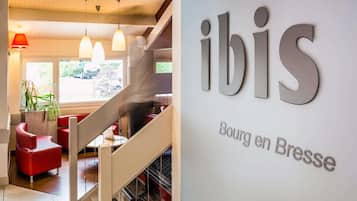 Een modern interieur met een trap, rode zitplaatsen en een bord met de tekst 'ibis Bourg en Bresse'.