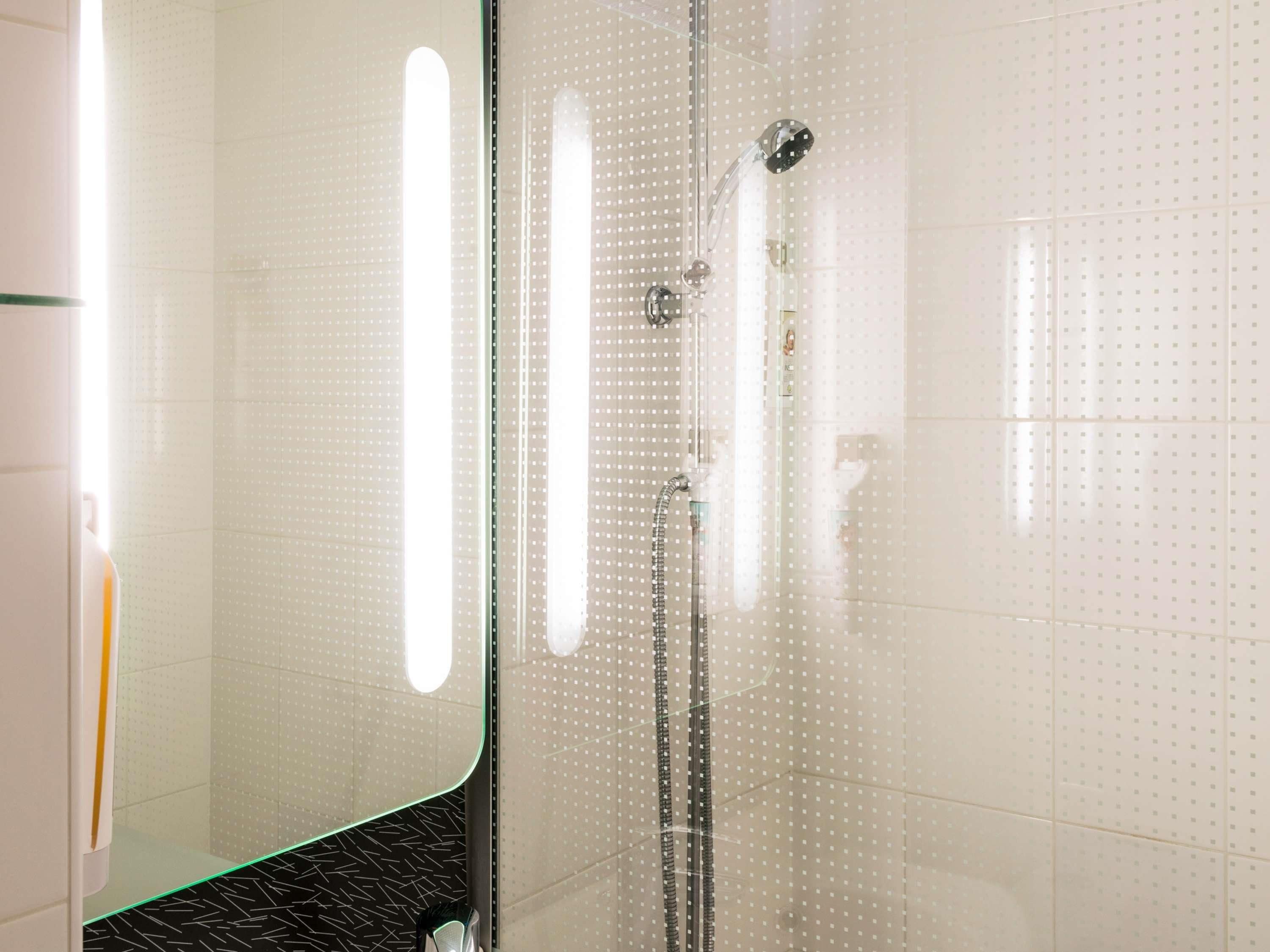 Un baño moderno con cabina de ducha de vidrio, cabezal de ducha visible y mampara de cristal.