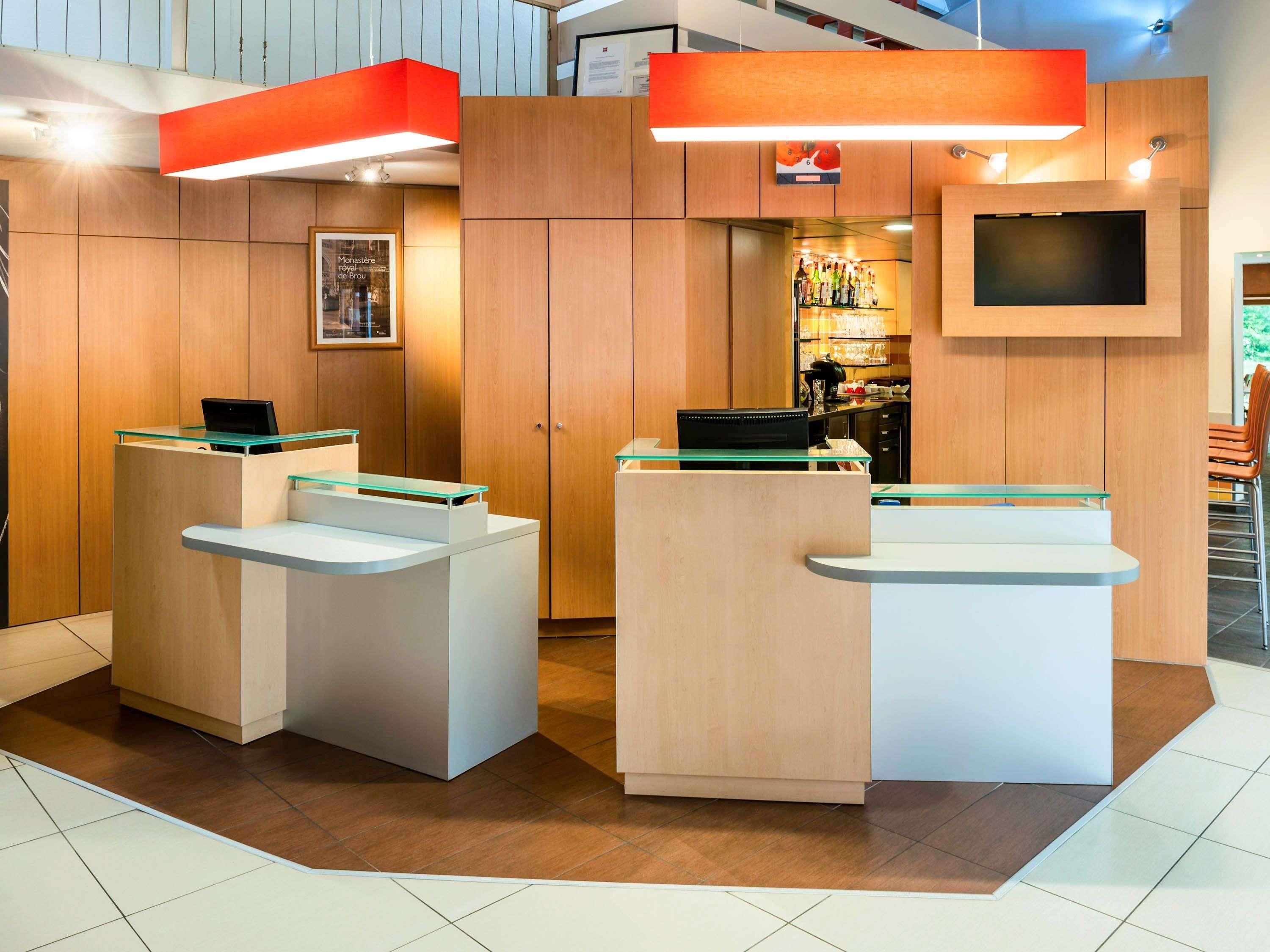 A reception area with two glass-top counters, wooden paneling, a mounted TV, and a visible bar area in the background.