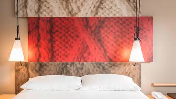 A hotel room with a bed, white pillows, a nightstand with a phone, and two pendant lights.