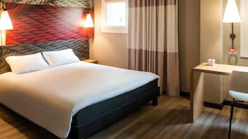 Een hotelkamer met een bed, bureau, stoel en een lamp.