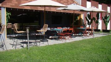 Une terrasse extérieure avec des tables et des chaises, des parasols et des plantes en pot.