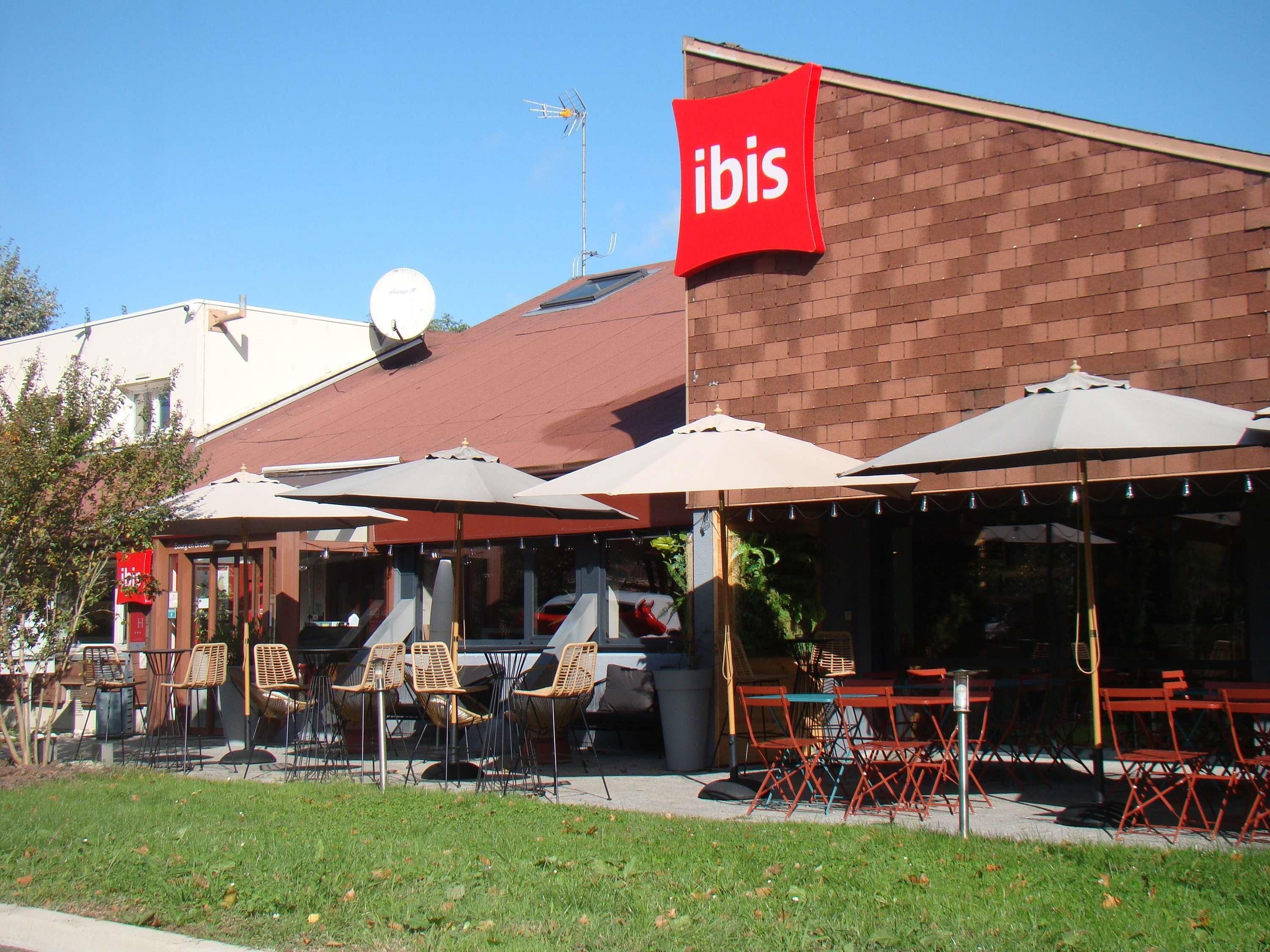 An outdoor seating area with umbrellas and chairs, a red 'ibis' sign, and a brick building facade.