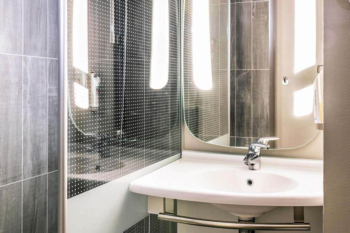 Un baño moderno con un espejo grande, un lavamanos blanco y un box de ducha.