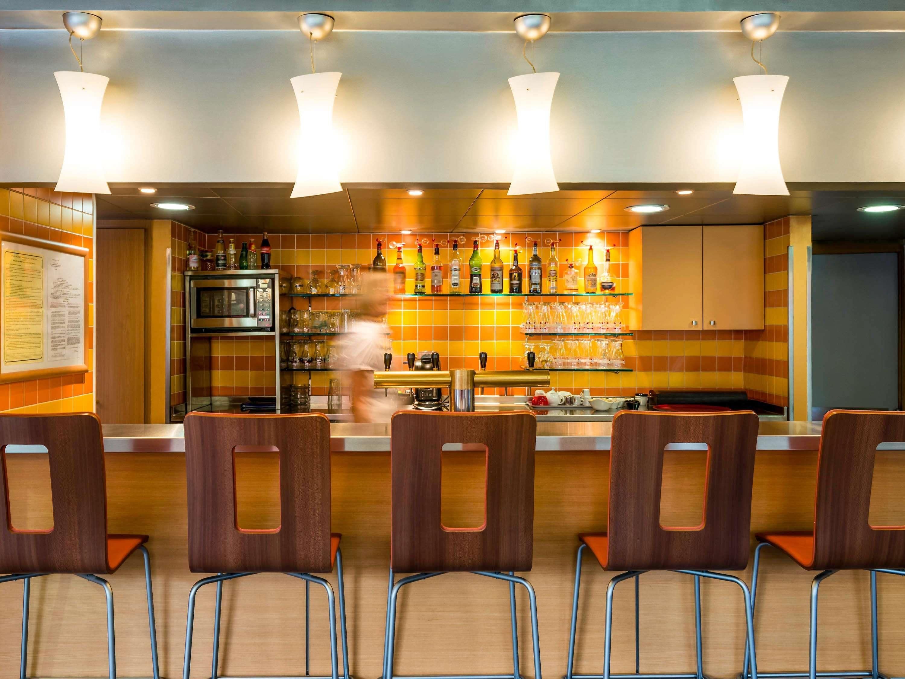 Een bar met een toonbank, planken vol flessen en stoelen.