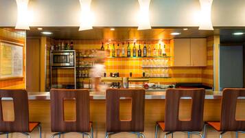 Een bar met een toonbank, planken vol flessen en stoelen.