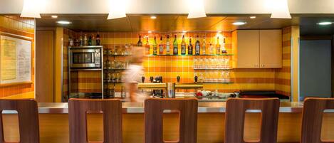 A bar area with a counter, shelves with bottles, and chairs.