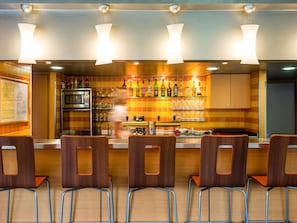 Zona de bar con mostrador, estanterías llenas de botellas y sillas.