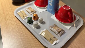 A tray with a red coffee machine, a blue canister, red cups, and various coffee pods on a wooden table. - ibis Bourg En Bresse (Bourg-en-Bresse)